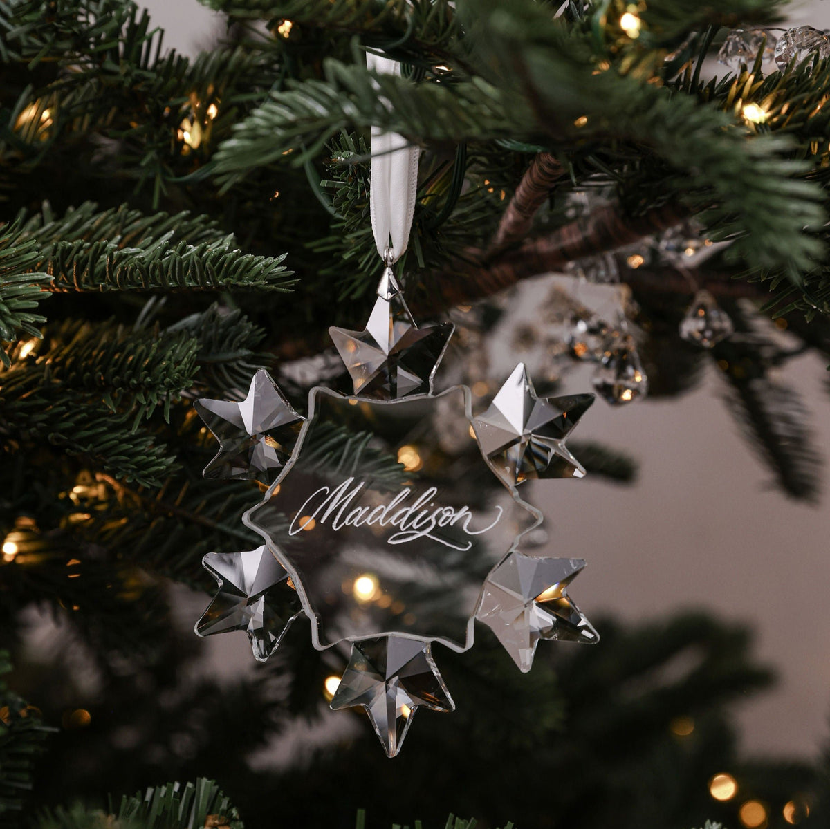Crystal snowflake bauble engraved with the name Maddison hanging on a Christmas tree