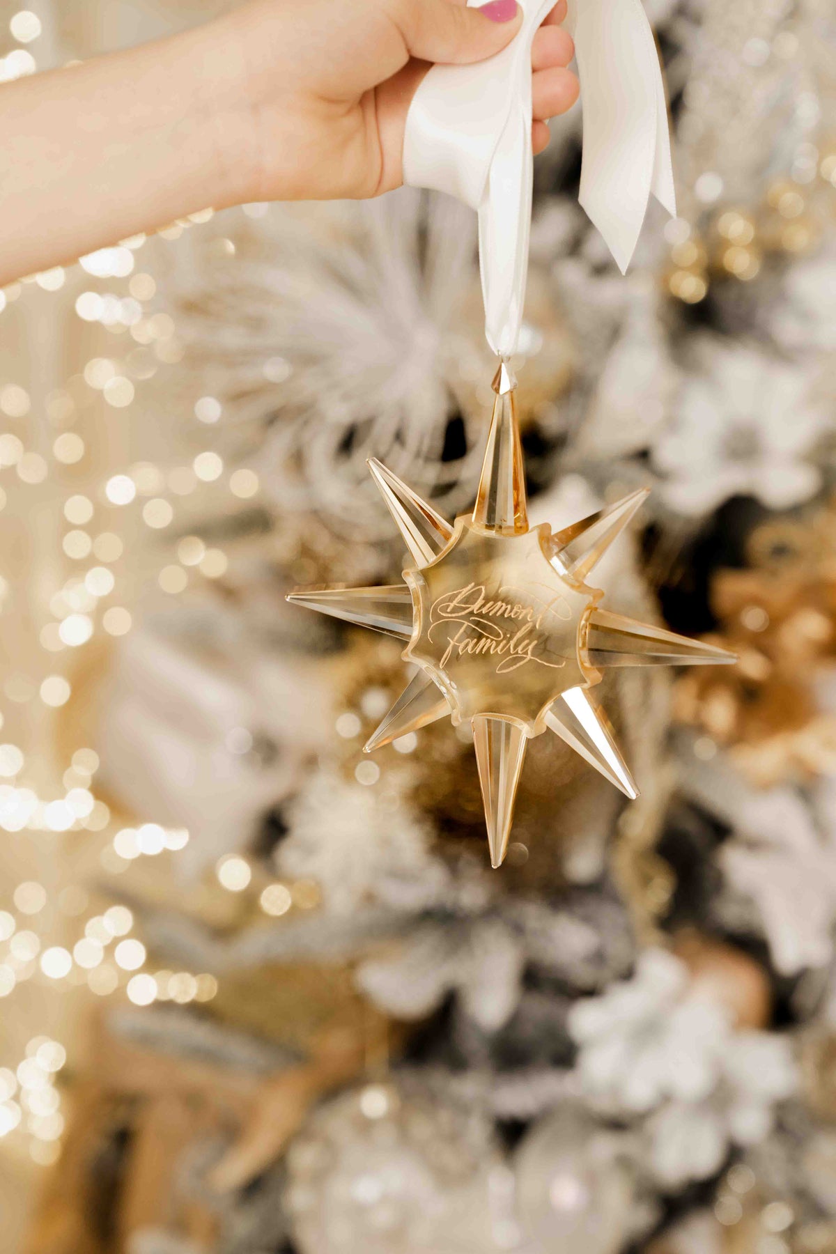 Hanging an engraved gold star ornament on a white Christmas tree