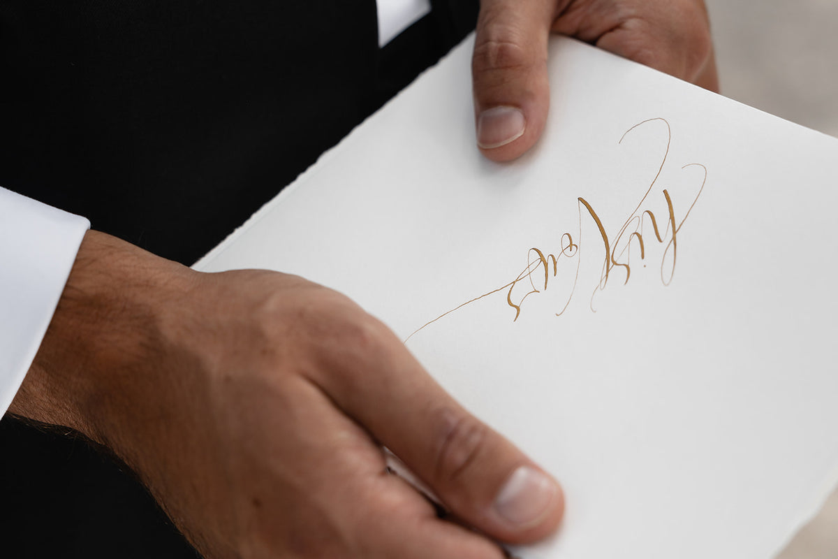 His vows calligraphy vow book in gold ink held by the groom