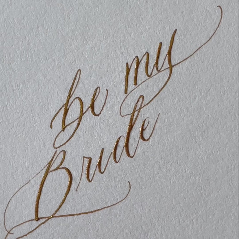 Gold ink, handwritten calligraphy being written on a bridesmaid proposal card