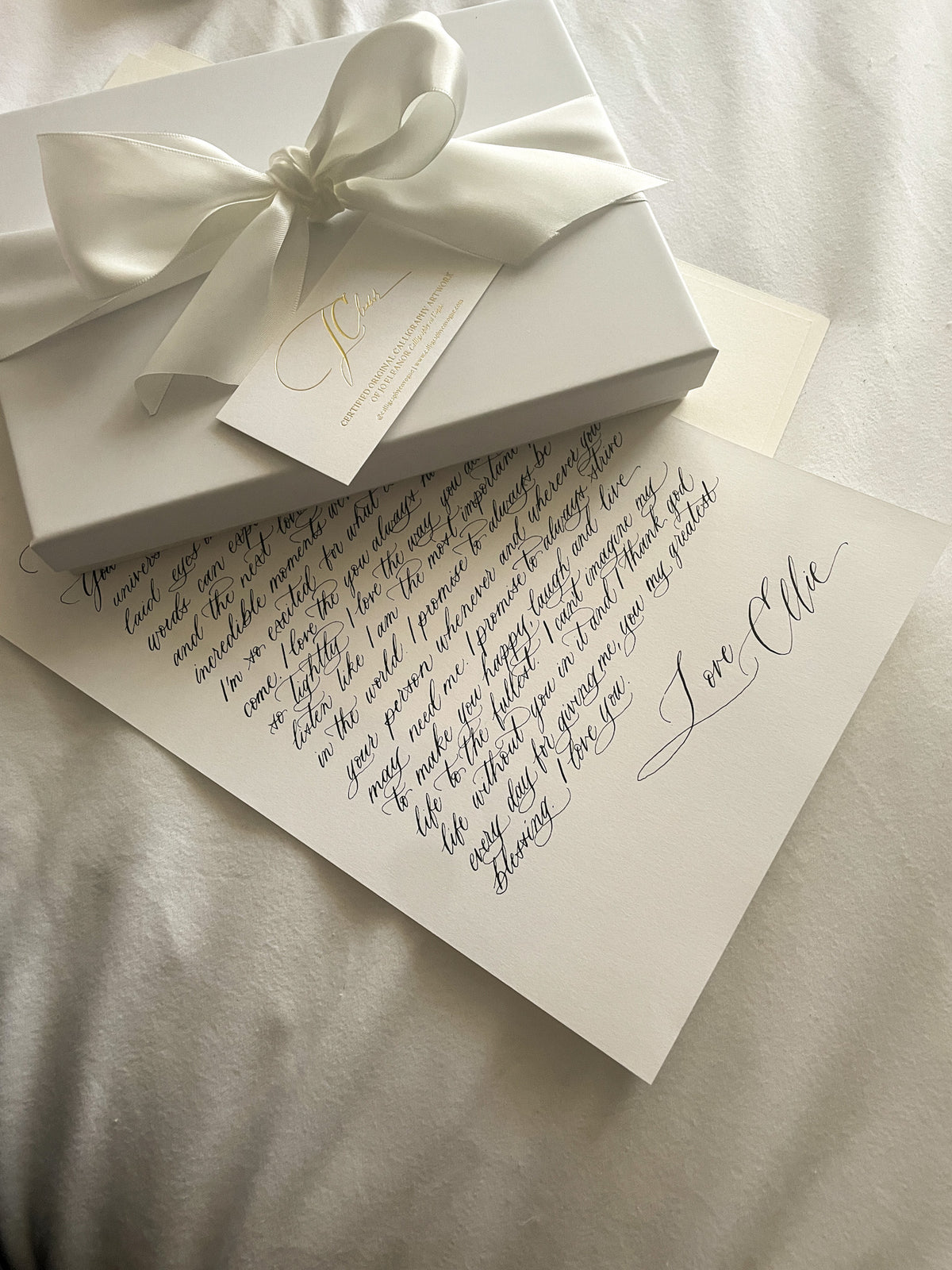 Calligraphy love letter beside a gift box tied with white ribbon