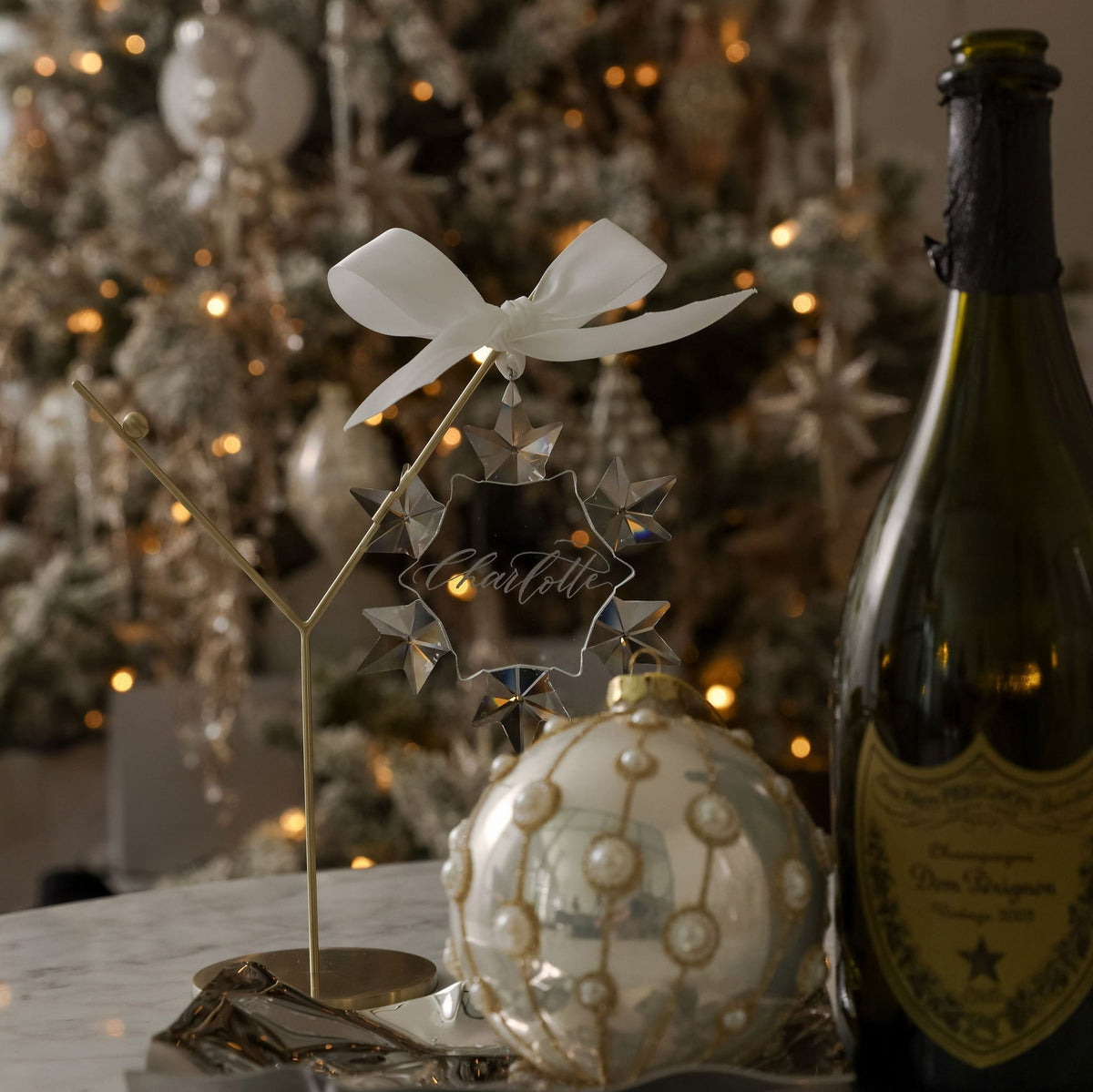 Hand-engraved crystal snowflake bauble on a stand beside a Christmas tree and champagne